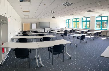 Es ist der große Seminarraum 6 des IHK-Bildungszentrums Bonn/Rhein-Sieg mit Medien, Tischen und Stühlen und einem Teppichboden zu sehen.
