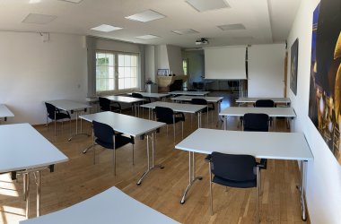 Der kleine Seminarraum 11 des IHK-Bildungszentrums Bonn/Rhein-Sieg mit Medien, Tischen, Stühlen und einem Teppichboden.