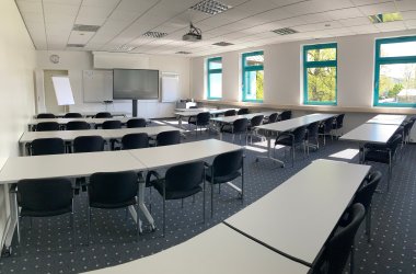 Der mittelgroße Seminarraum 1 des IHK-Bildungszentrums Bonn/Rhein-Sieg mit Medien, Tischen, Stühlen und einem Teppichboden.