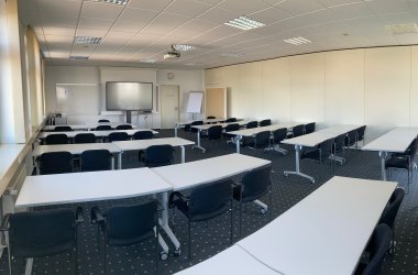 Der mittelgroße Seminarraum 2 des IHK-Bildungszentrums Bonn/Rhein-Sieg mit Medien, Tischen, Stühlen und einem Teppichboden.