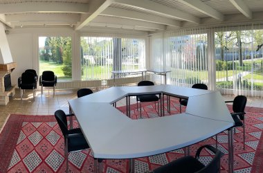 Der Wintergarten des IHK-Bildungszentrums Bonn/Rhein-Sieg mit Medien, Tischen, Stühlen und einem Teppichboden.