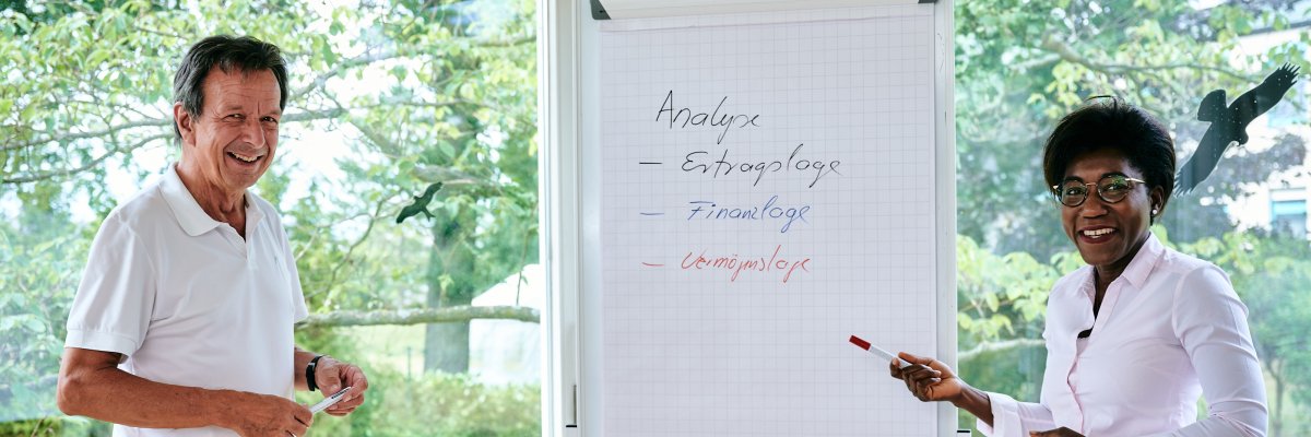 Zwei Dozenten stehen vor einem Flipchart und erklären etwas